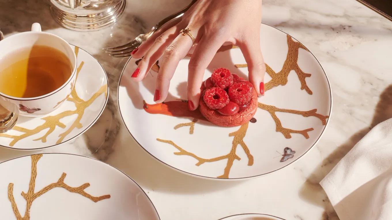 Some details of the tea time with a hand taking a raspberry cookie of Cédric Grolet next to hot drinks and a peach, at Le Meurice, Paris