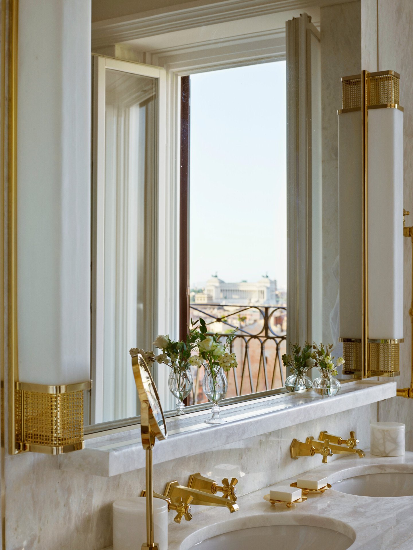 White marble bathroom with double sinks and view of Vittoriano reflected in mirror inside Presidential Suite at Hotel Eden, Rome 