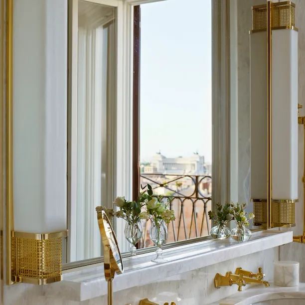 White marble bathroom with double sinks and view of Vittoriano reflected in mirror inside Presidential Suite at Hotel Eden, Rome