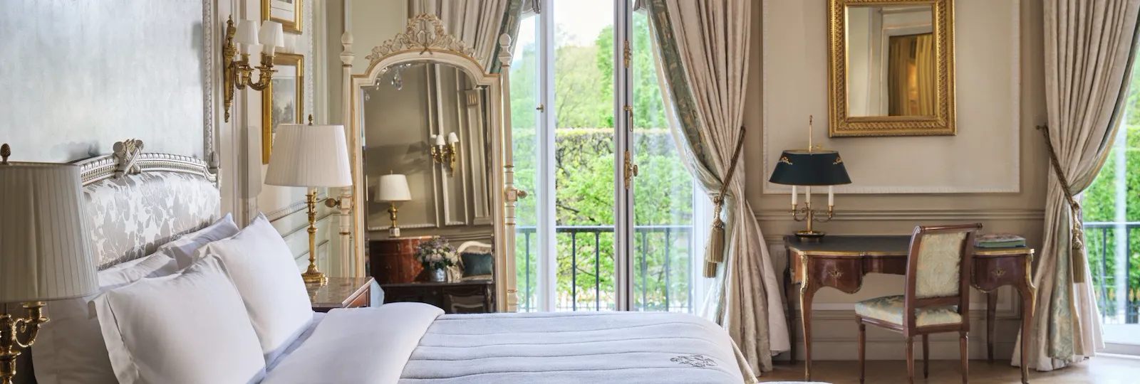 Large view of the right side of the bed with the mirror, the desk, the chair and the windows open behind, at Le Meurice, Paris