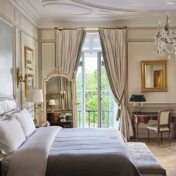 Large view of the right side of the bed with the mirror, the desk, the chair and the windows open behind, at Le Meurice, Paris